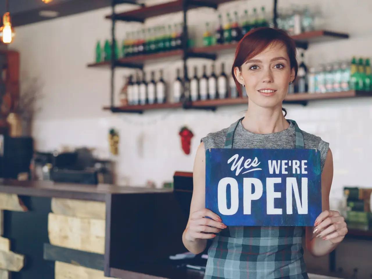 A cafe owner holding an open sign at her counter