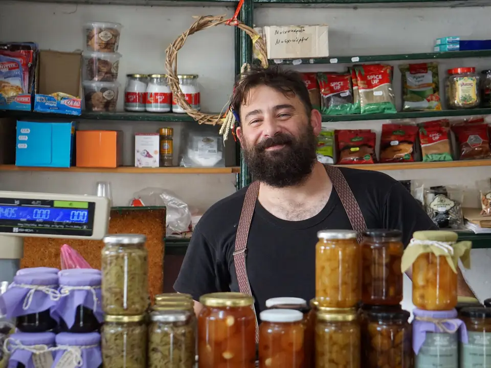 Shopkeeper behind the counter of a small food shop with preserves