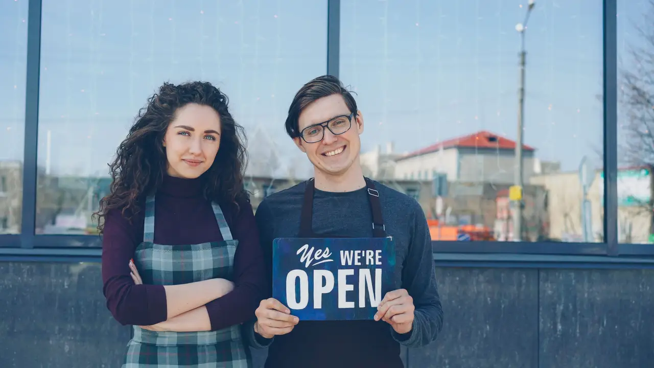 Cafe owners holding a blue open sign outside their shop
