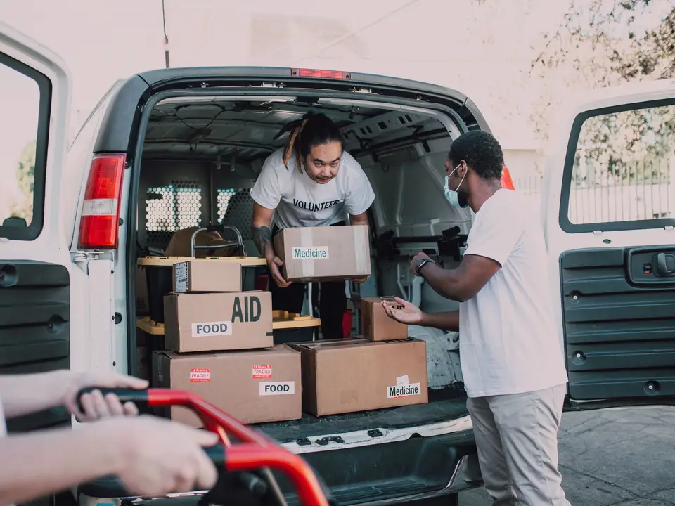 Volunteers unloading boxes labeled food and medicine from a van for charity