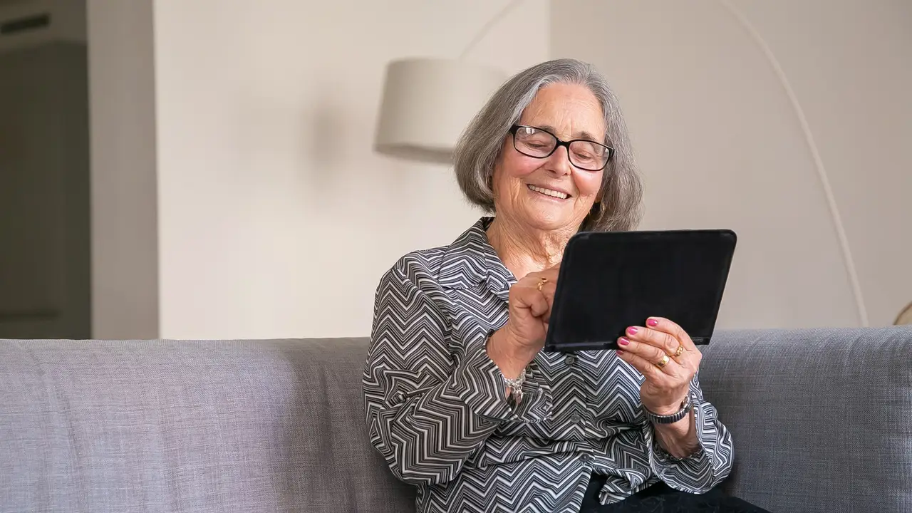 Older woman smiling at a tablet on a sofa at home