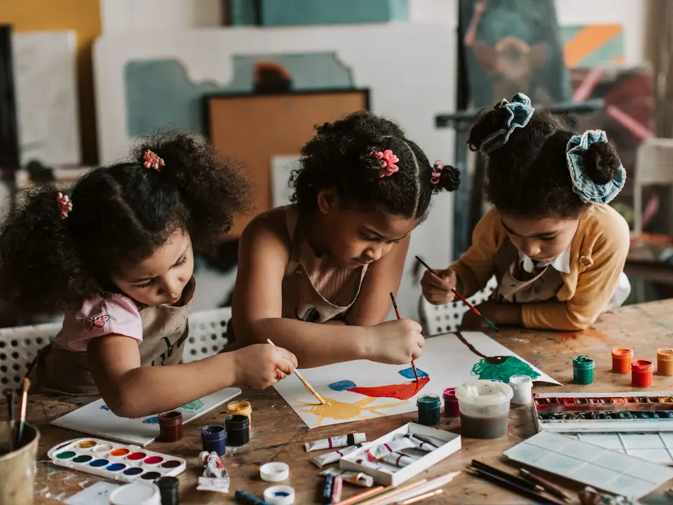 Three young girls engaged in painting at an art table, expressing creativity and teamwork