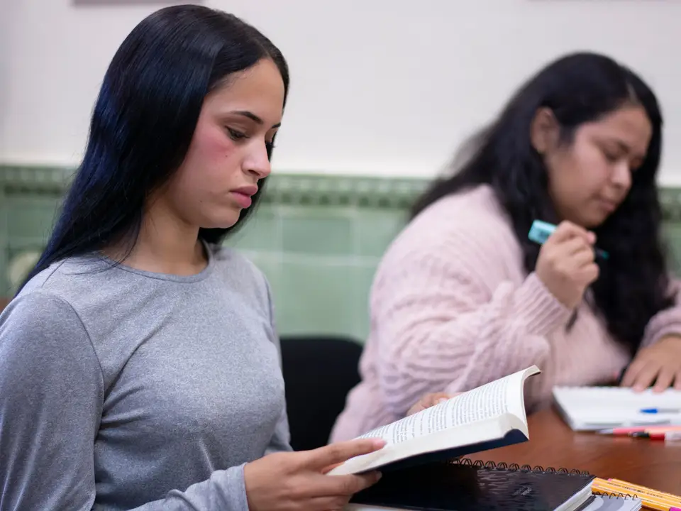 Two female students focus on reading and taking notes during a class session