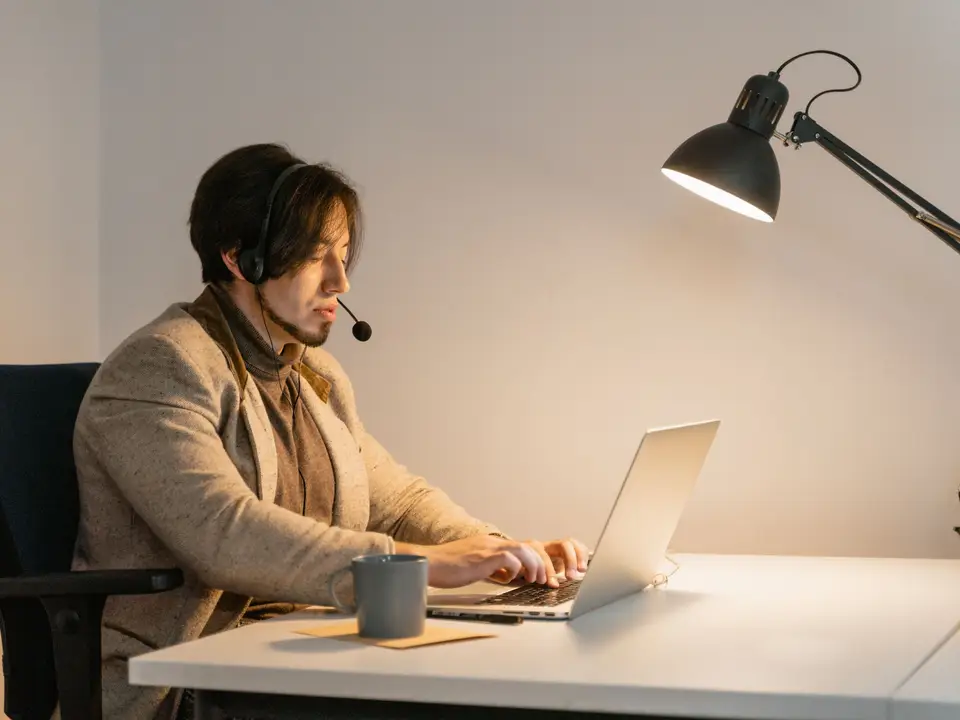 Agent in a headset typing replies on a laptop under a desk lamp