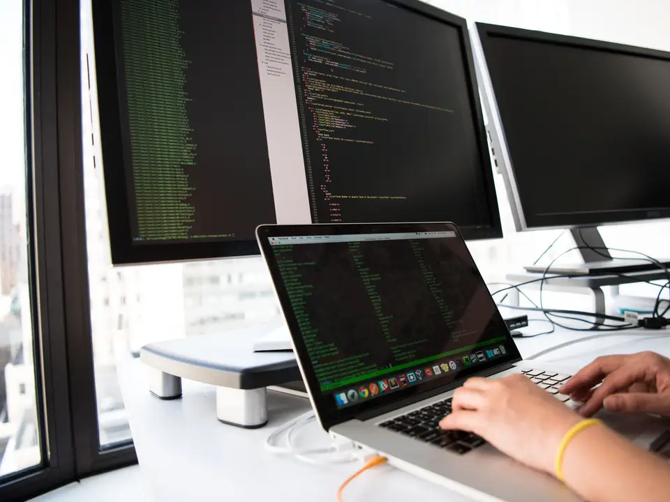 Developer writing code on a laptop in front of several monitors