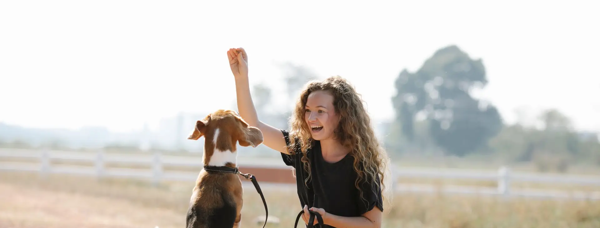 A smiling woman in a grey sweater teaching her dog to sit up and beg with a treat