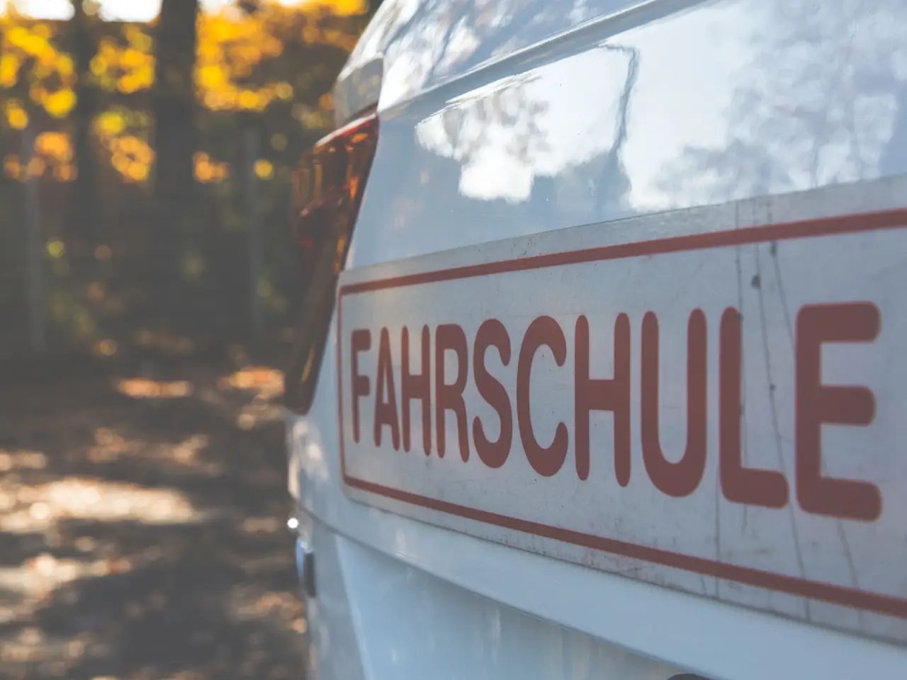 White driving school car with a Fahrschule sign in autumn foliage