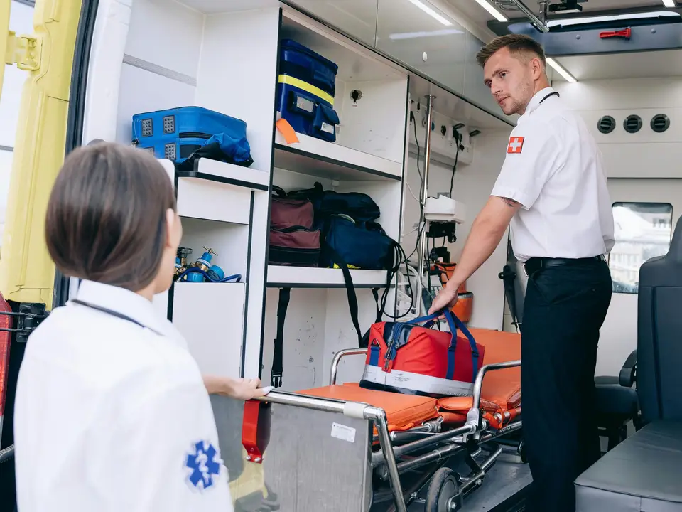 Paramedic taking an aid bag from a gurney beside an ambulance