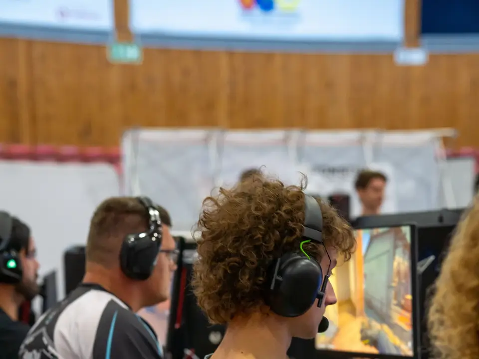 Players wearing headsets at a competition with colourful game graphics on monitors