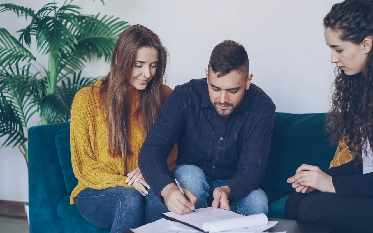 A young couple signing paperwork with their planner on a sofa