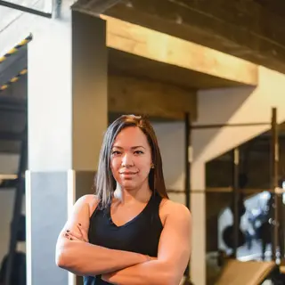 Fit woman in gym attire confidently posing with arms crossed indoors.