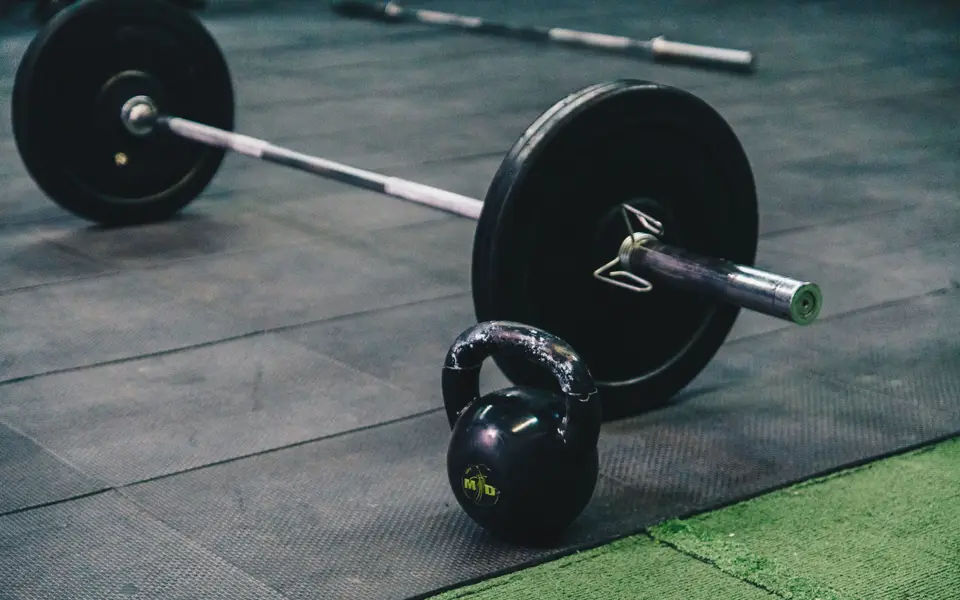 Barbell and kettlebell on gym floor, ideal for fitness and strength training themes.