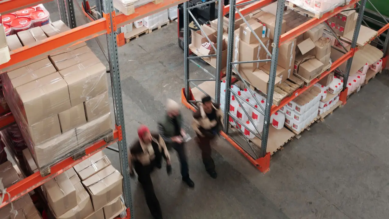 Workers moving stacked cases past tall warehouse racks
