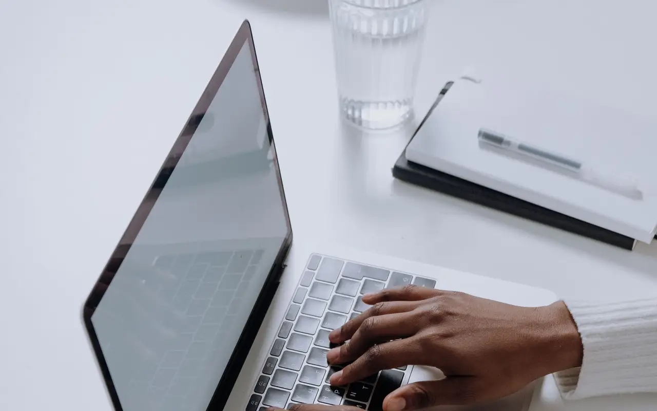 Hands typing on a laptop at a white desk