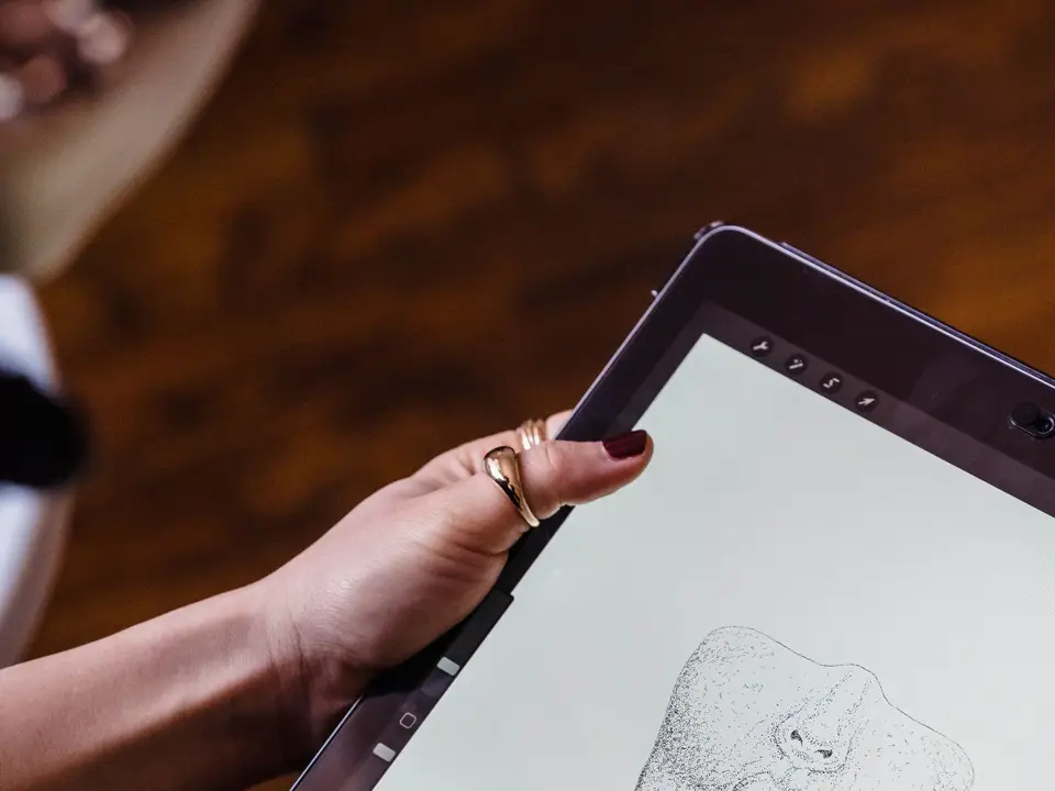 Hands holding a stylus over a tablet while sketching a character's face