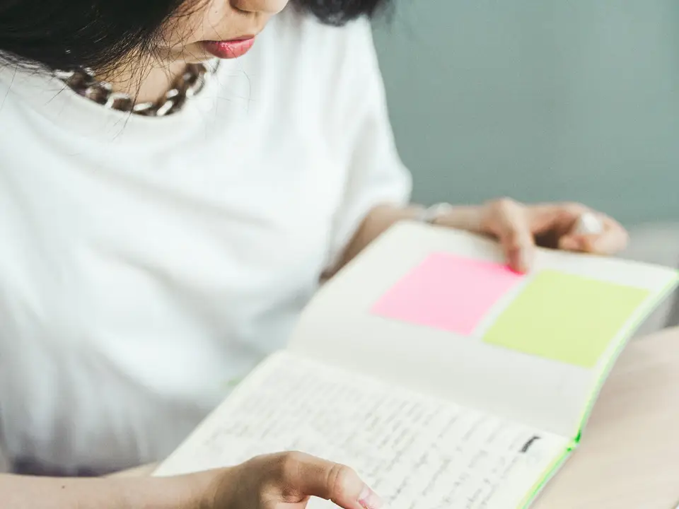 Woman writing notes in a notebook beside a laptop