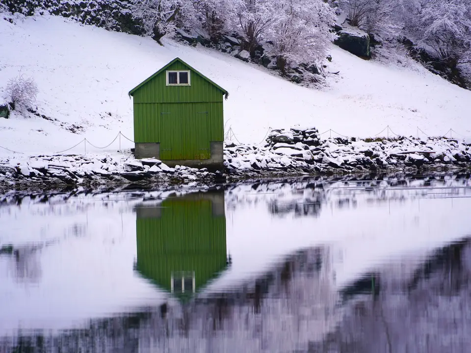 Snow on the lodge roof beside still water
