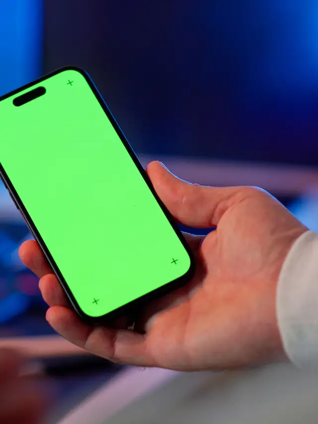 Hand holding a smartphone with a bright app home screen in a design studio