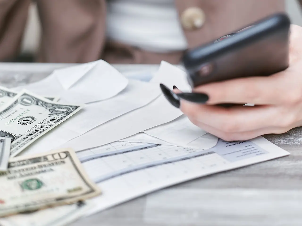 Hands holding a smartphone above a desk with documents and banknotes