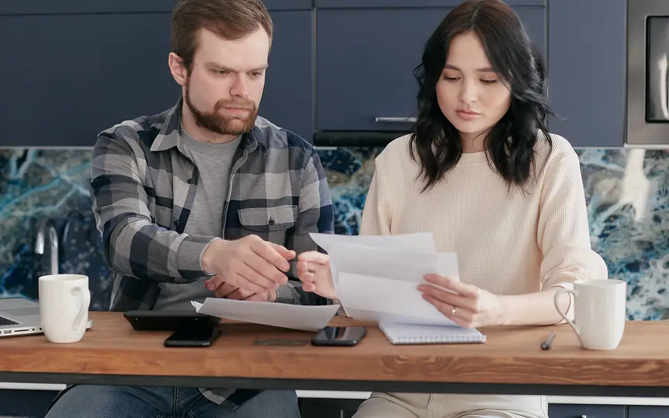 A couple at a wooden table working through bills and paperwork