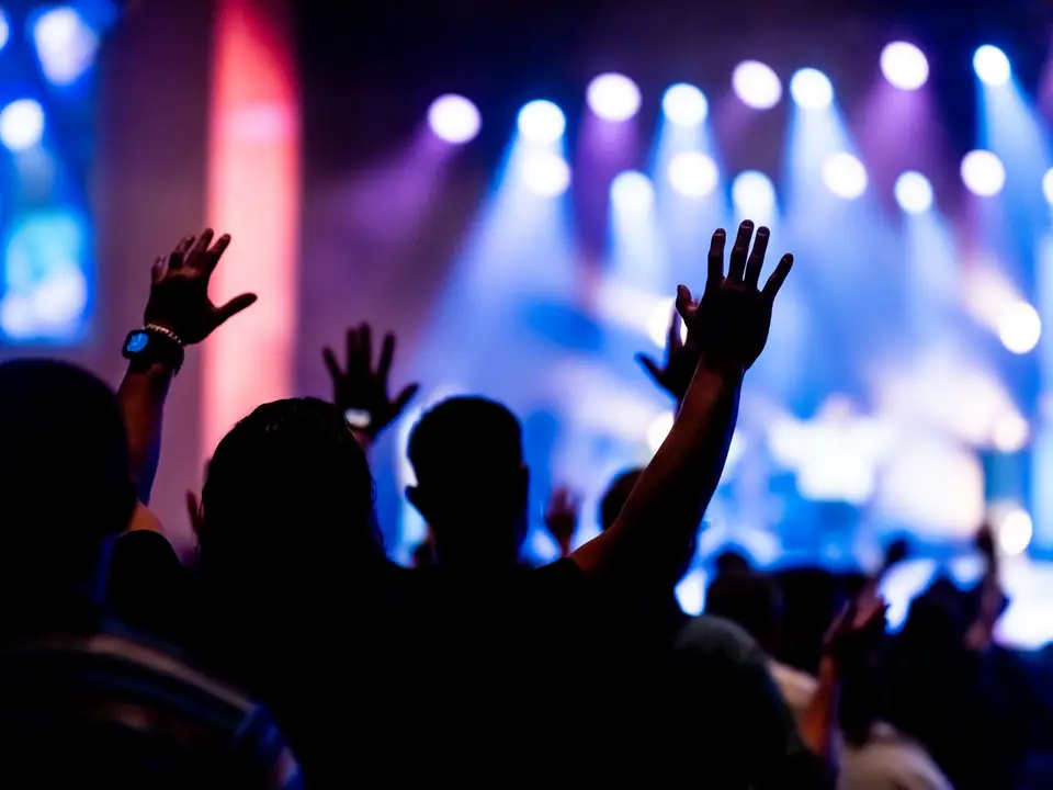Audience with raised hands facing a stage lit in blue and purple