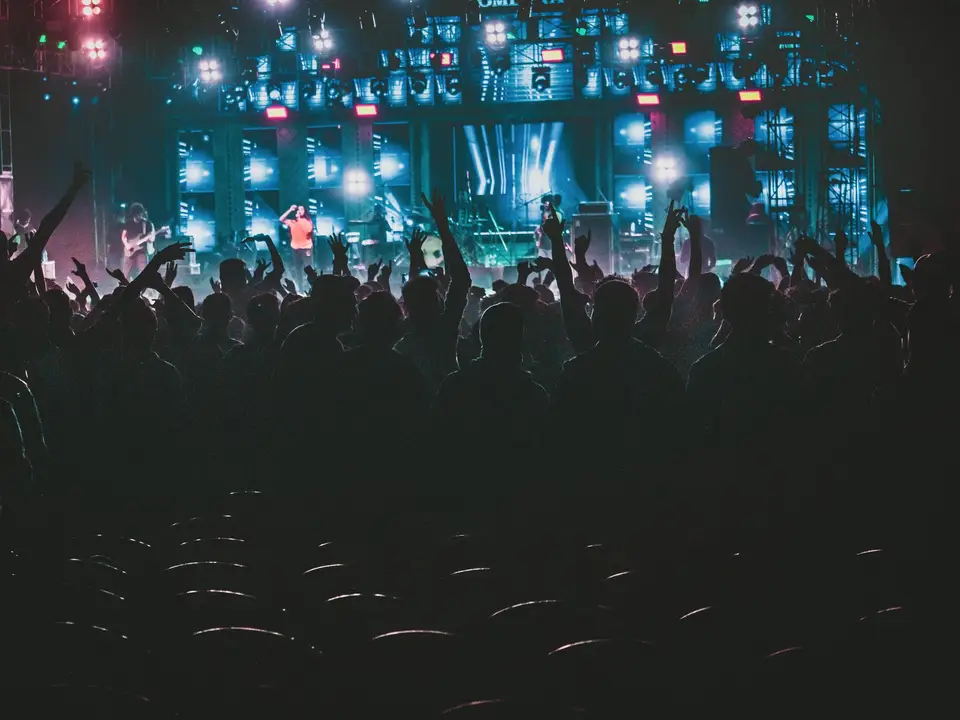 Large crowd in silhouette facing a stage with bright white spotlights