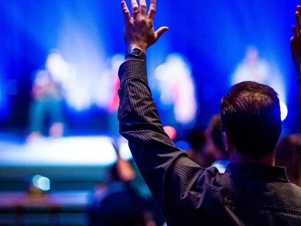 Fan with a raised hand at a concert looking at a bright blurred stage