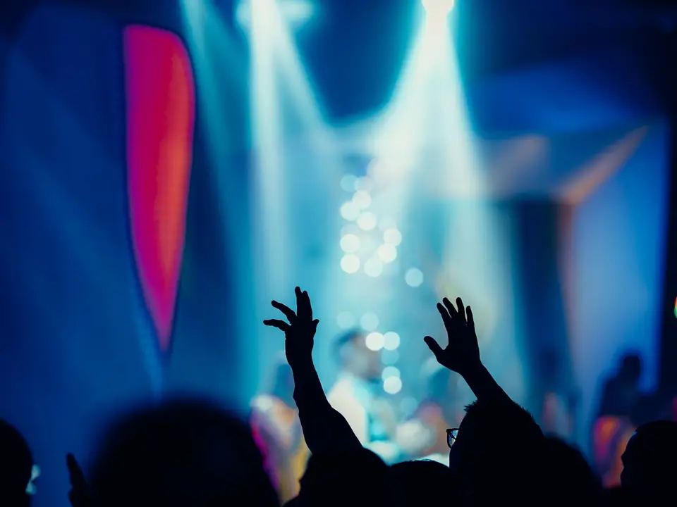 Silhouetted hands raised against hazy blue and pink concert lights