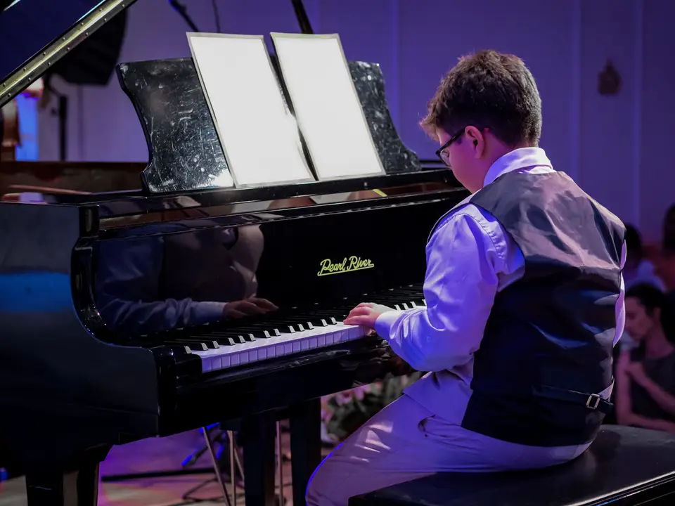 Young boy playing a grand piano during a recital