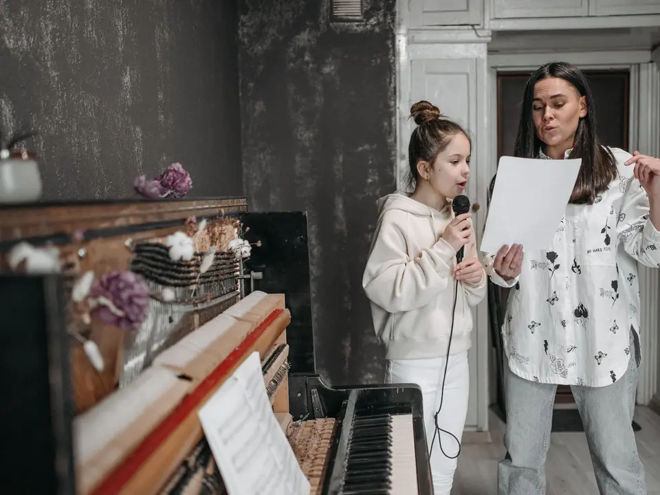 Girl taking a voice lesson, singing into a microphone by a piano