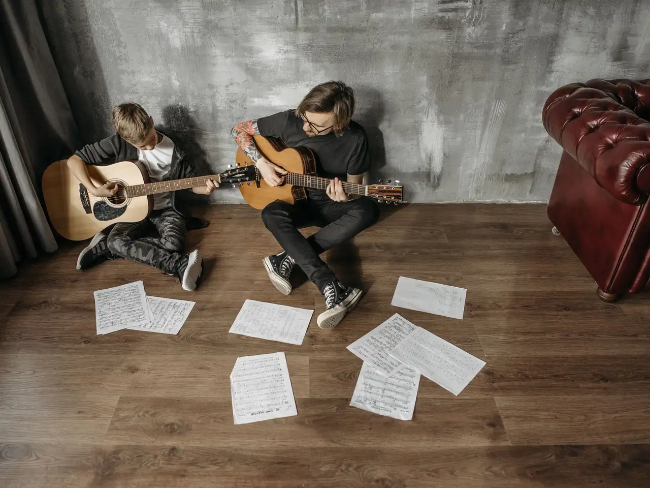 Adult and teenager practicing guitars with sheet music on a wooden floor