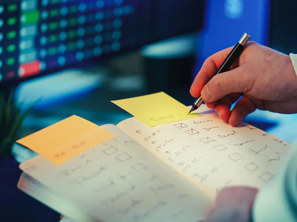 Person writing in a planner next to a task checklist