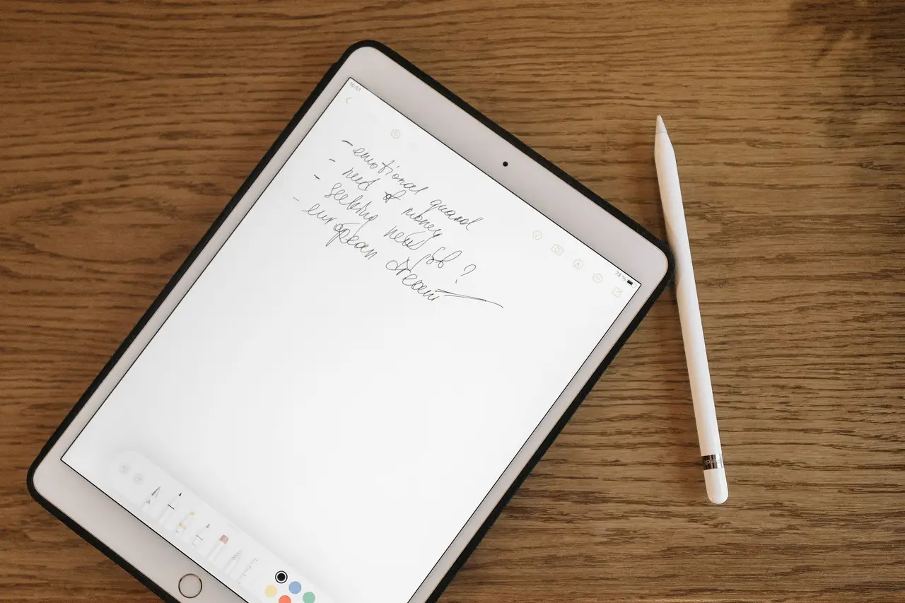 Hand writing in a notebook on a tablet beside a fern plant and coffee