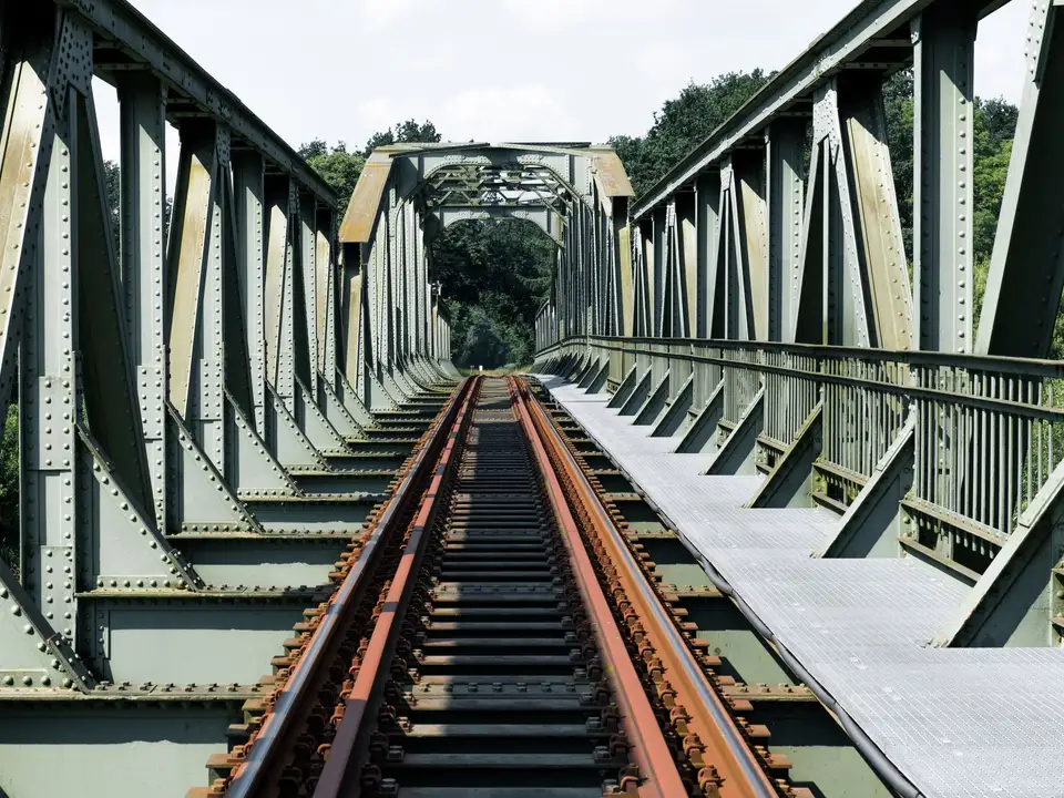 Railway track crossing a large green steel truss bridge