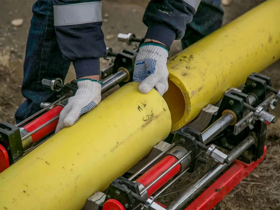 Workers in gloves joining large yellow pipes with hydraulic equipment