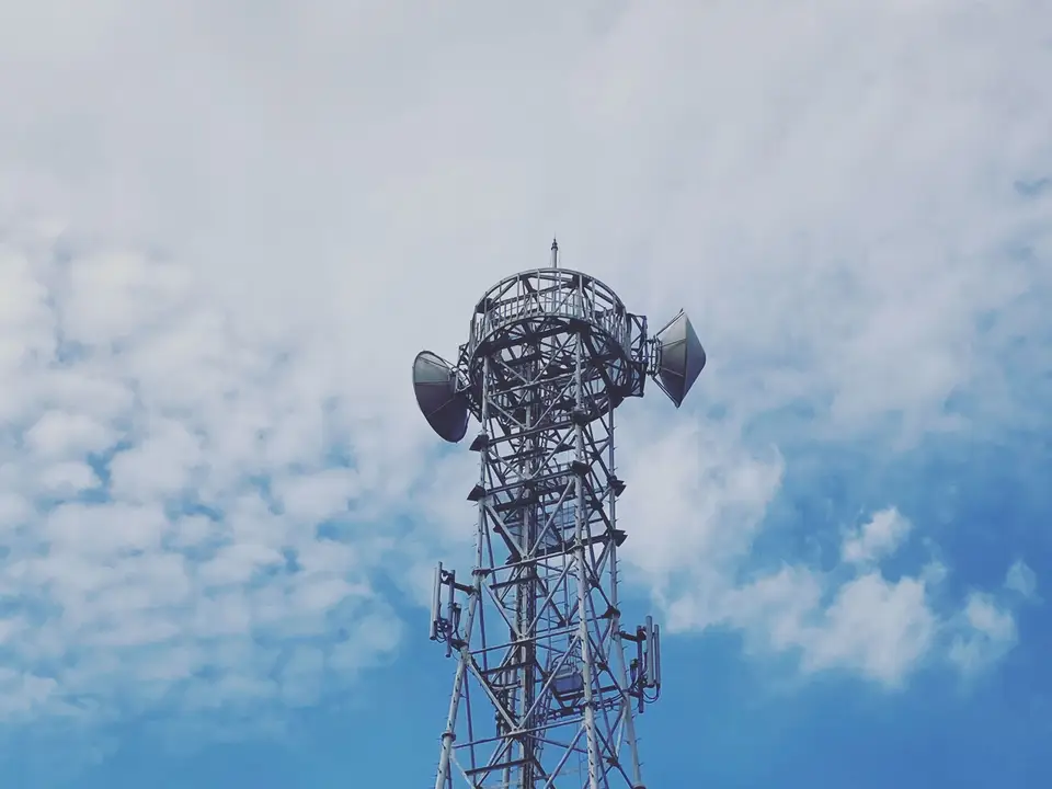 Looking up at a lattice radio tower against a blue sky with clouds