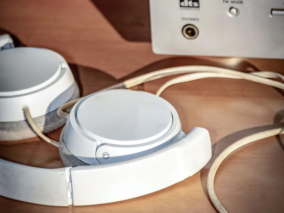 Headphones and a cable lying next to a vintage stereo receiver on a wooden table