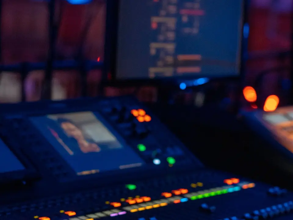 Digital mixing console in a dim studio with monitors showing audio software