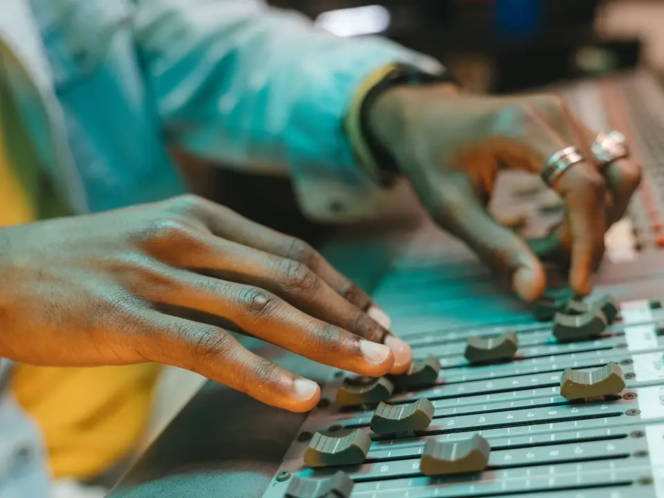 Producer's hands adjusting sliders and knobs on a mixing board