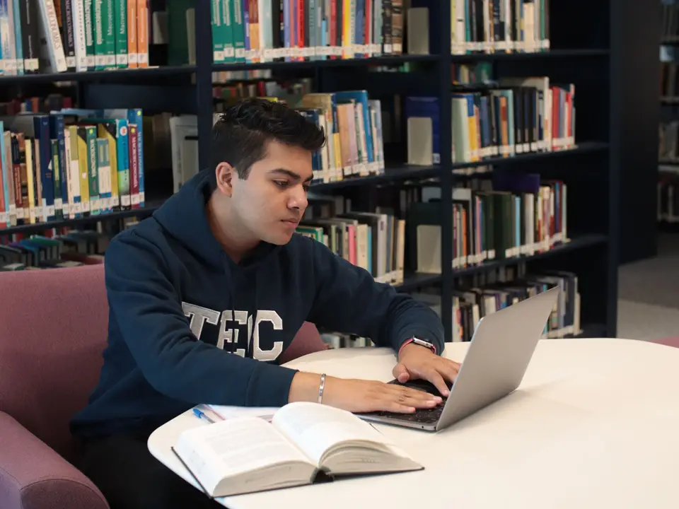 Student in library using laptop and textbooks for study and research