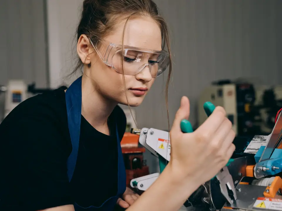 Focused female engineer using pliers in a workshop setting while wearing protective goggles