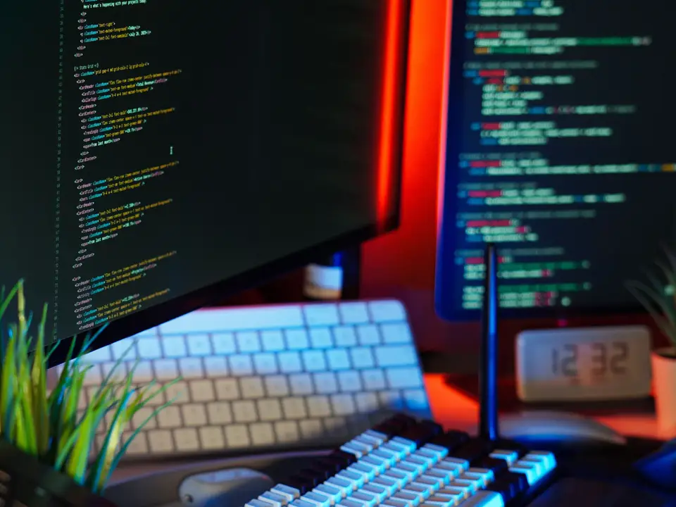 Workspace with monitors showing code, a keyboard and tech accessories