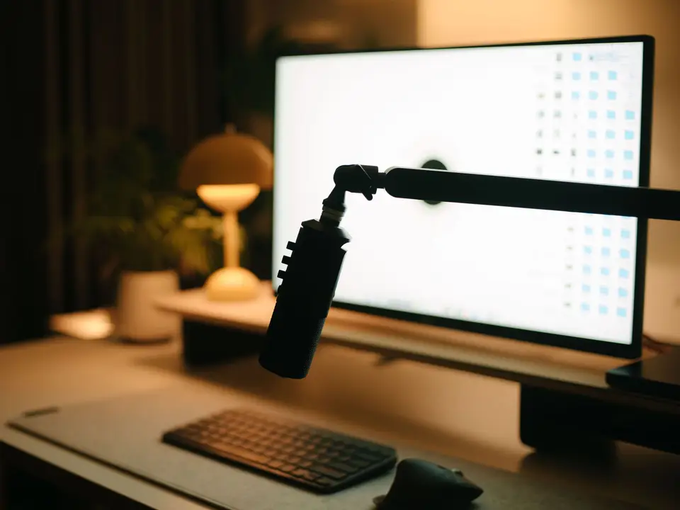 Warm desk setup with a large monitor, boom-arm microphone and desk lamp