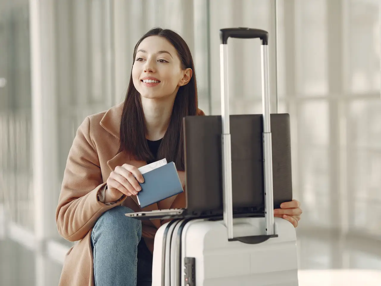 Woman with a laptop, luggage and passport in an airport terminal
