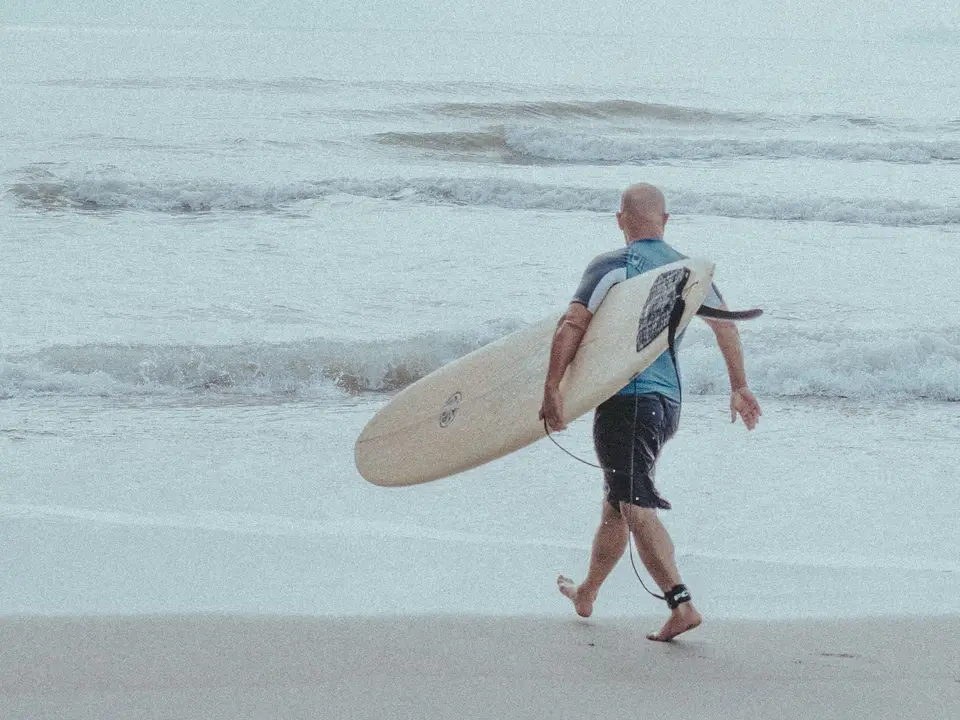 Surfer walking toward ocean with board