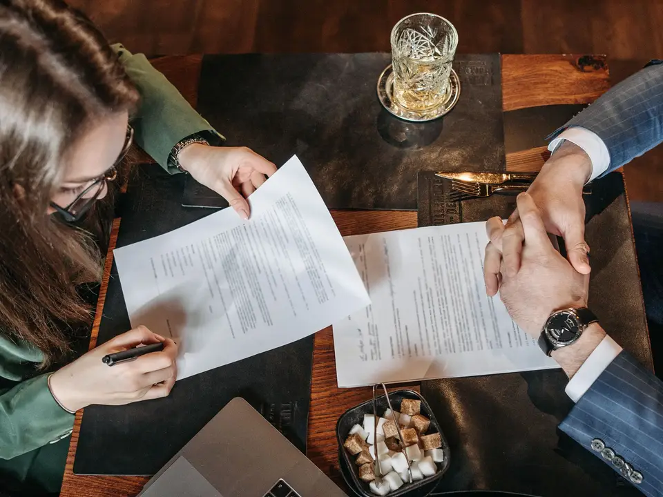 Top-down view of two people signing documents at a table with a laptop
