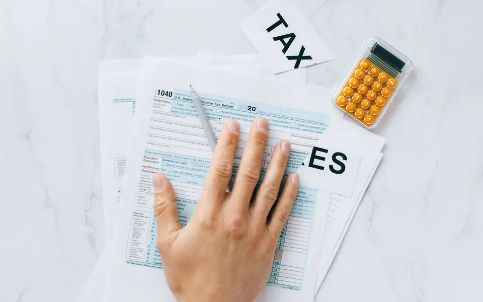 A hand holding a pen on a Form 1040 beside a calculator