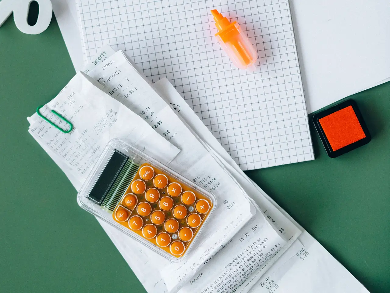 A taxes notebook with receipts, coins and a magnifying glass on a green desk