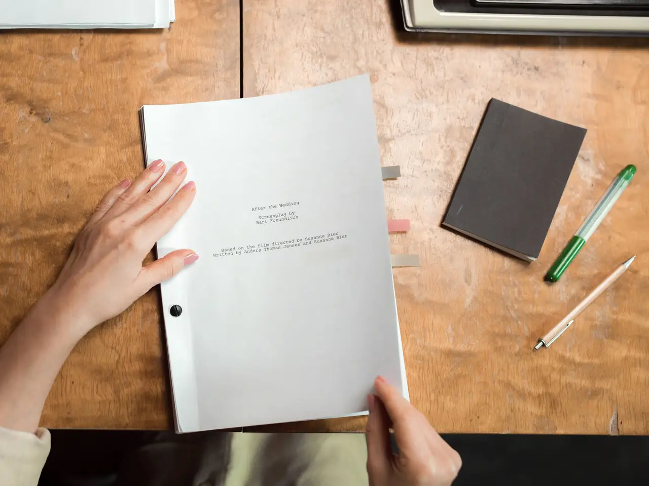 Hands sorting printed documents on a wooden desk with a pen and notebook