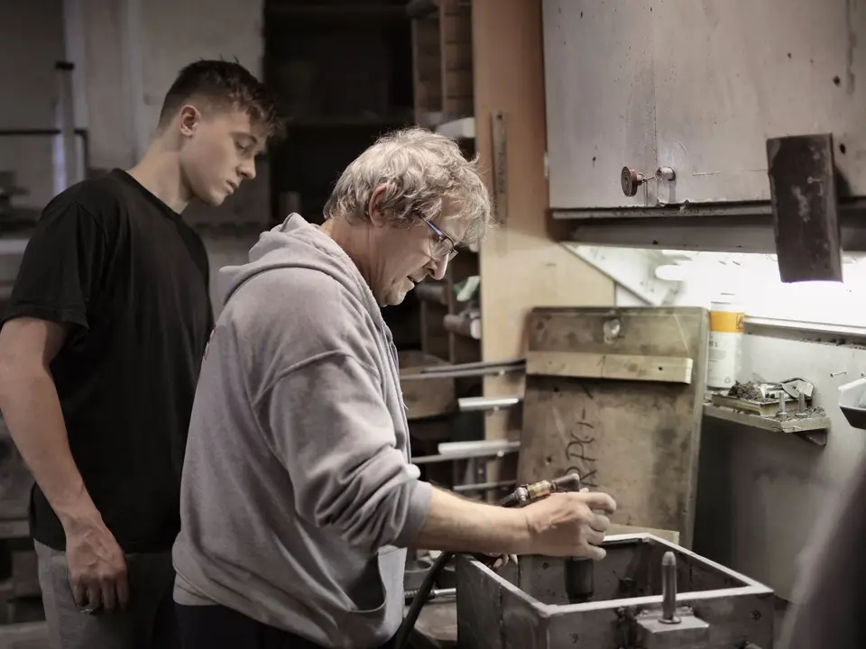 Experienced craftsman teaching a young apprentice in a workshop